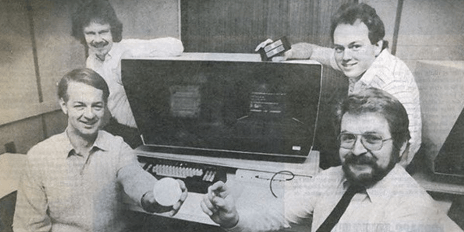 4 men sitting around an old computer