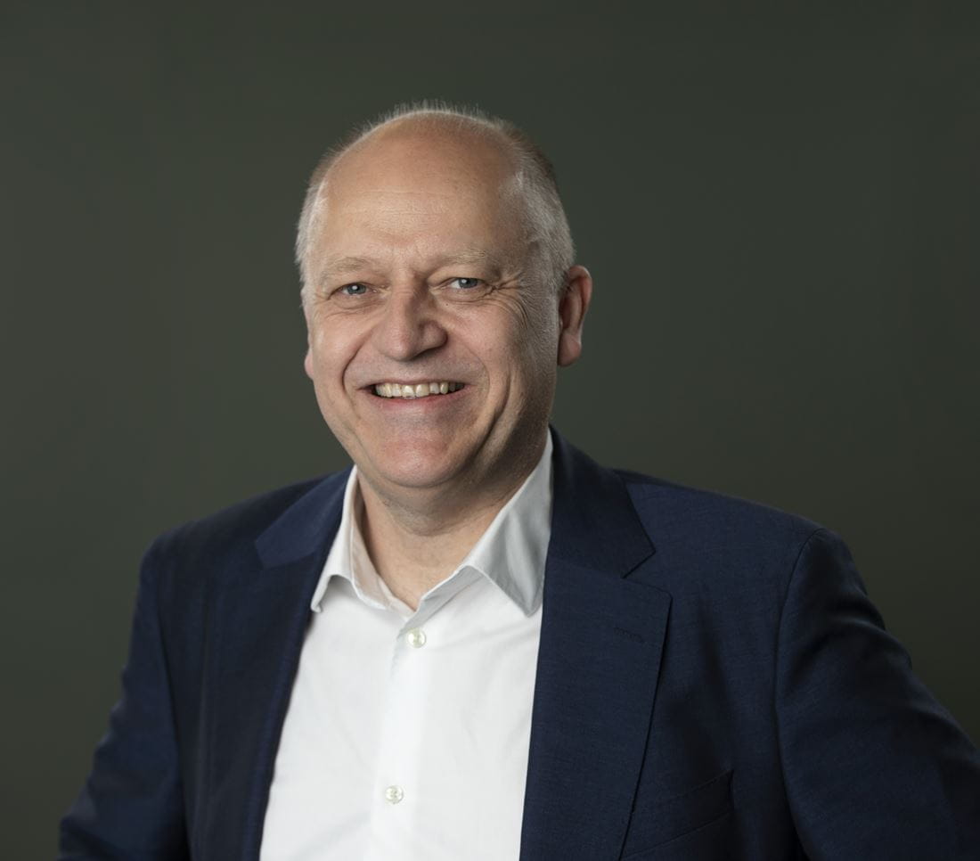 a man wearing a suit and tie smiling at the camera